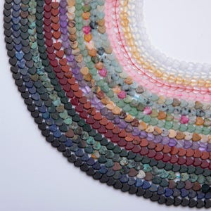 May include: A collection of heart-shaped beads in various colors, including black, blue, green, red, and pink. The beads are strung together, creating a curved arrangement against a white background. Ideal for jewelry making.