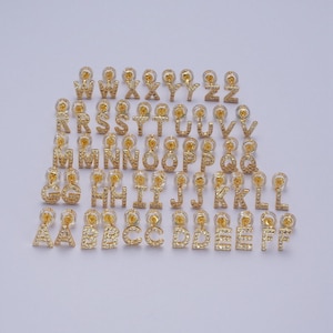 May include: A set of 26 gold-tone earrings, each featuring a different letter of the alphabet, adorned with sparkling clear rhinestones. The earrings are arranged in alphabetical order.