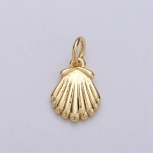 May include: A gold-colored seashell pendant with a loop for a necklace. The pendant has a detailed, textured surface with radiating lines and a scalloped edge. The pendant is likely made of metal.