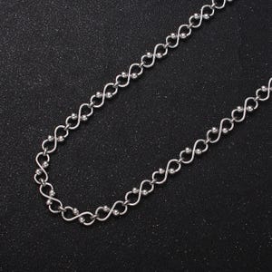 May include: A silver chain necklace with a unique, linked design. The chain is made of small, round beads connected by a series of loops.