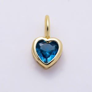May include: A heart-shaped pendant featuring a deep blue gemstone set in a polished yellow gold frame. The pendant includes a small, smooth gold bail at the top for attachment to a chain, showcasing a clean, symmetrical design with a vibrant blue center.