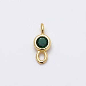 May include: A gold-colored pendant with a round, dark green gemstone set in the center. The pendant has a loop at the top for a chain and a smaller, oval-shaped loop at the bottom. The design is simple and elegant.