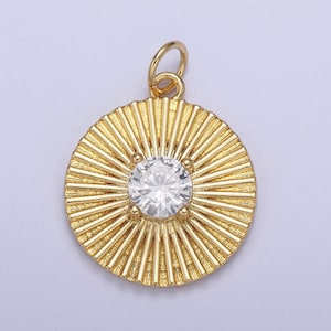 Puede incluir: Colgante dorado con una gema redonda y transparente en el centro. El colgante tiene un diseño de rayos de sol con líneas radiales que emanan de la gema. Un pequeño lazo en la parte superior para una cadena.