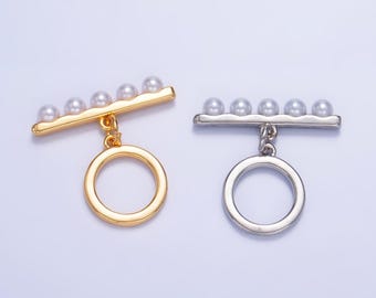 May include: Two gold and silver toggle clasps with a row of five faux pearls and a dangling ring.