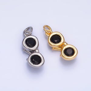 May include: Two small sunglasses charms, one silver-toned and one gold-toned. Each charm features two round frames with black gemstone lenses. The charms are designed for jewelry making, such as necklaces or bracelets.