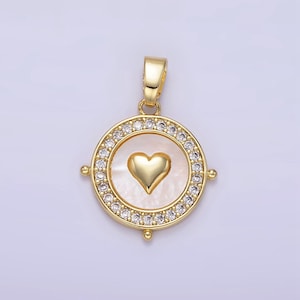 May include: A gold pendant with a white heart-shaped shell in the center. The shell has a gold heart in the center. The pendant is surrounded by a circle of small clear stones.