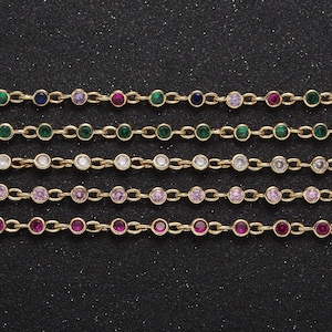 May include: Five gold chains with different colored gemstones. The chains are arranged in a row, with the top chain having green, blue, pink, red, and green gemstones. The second chain has all green gemstones. The third chain has clear gemstones. The fourth chain has pink gemstones. The fifth chain has red gemstones.