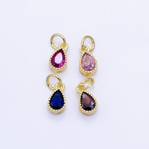 May include: Four gold-plated teardrop charms, each with a different coloured gemstone: pink, purple, blue, and red. The charms have a small loop at the top for attaching to a chain or bracelet. The charms are displayed on a white background.