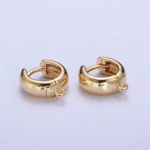 May include: Two gold-coloured hoop earrings. Each earring features a rounded, thick design with a small loop at the base. The earrings are presented against a white backdrop, emphasising their shiny, metallic finish. These earrings are suitable for everyday wear.