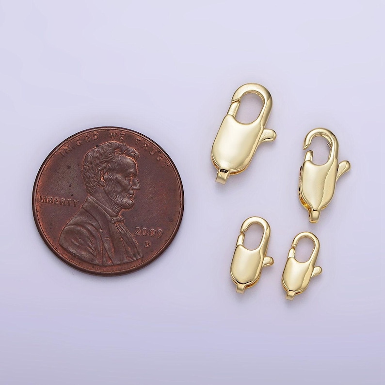 May include: Four gold-toned lobster claw clasps, a type of jewelry finding, are shown on a white surface. The clasps are different sizes, with the largest one being about the size of a US penny.