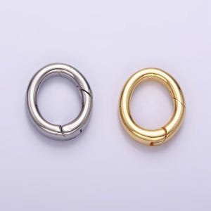 Könnte beinhalten: Zwei Metallringe, einer silberfarben und einer goldfarben, mit einem Federverschluss. Die Ringe haben einen Durchmesser von etwa 2,5 cm.