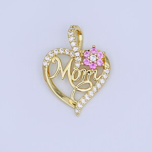 May include: A gold-colored pendant in the shape of a heart with the word "Mom" in cursive script. The heart is outlined with small, clear gemstones. A small flower with pink gemstones is on the upper right side of the heart.
