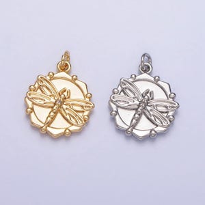 May include: Two silver and gold pendants with a dragonfly design. The dragonfly is detailed with a small clear stone in the center.