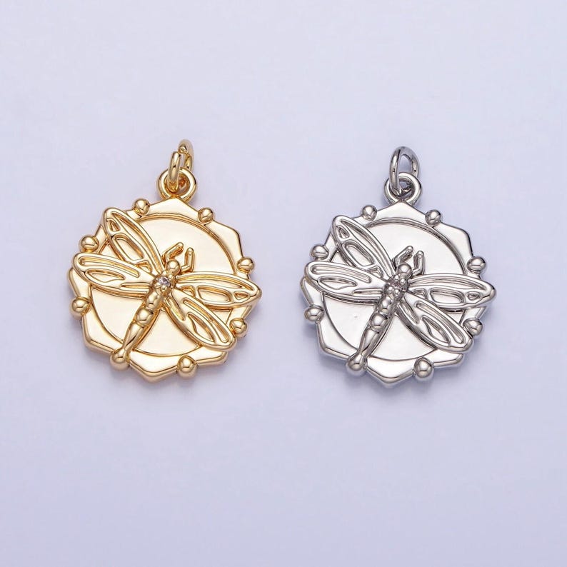 May include: Two silver and gold pendants with a dragonfly design. The dragonfly is detailed with a small clear stone in the center.