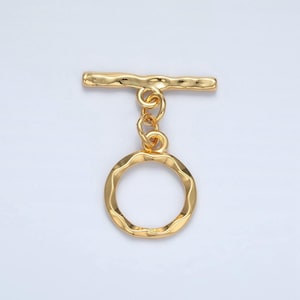 May include: Gold-toned metal toggle clasp with a round, textured ring. The clasp is designed for attaching to jewelry or other accessories.