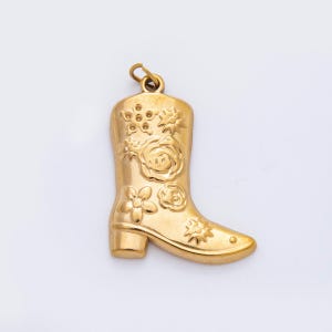 May include: A gold-colored pendant in the shape of a cowboy boot. The boot is decorated with floral designs, including roses and other flowers. The pendant has a loop at the top for attaching to a chain or bracelet.