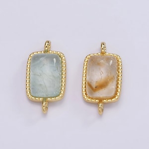 May include: Two gold-toned pendant charms with a rectangular shape. The charms feature a clear stone with a gold-toned border. One stone is light blue and the other is clear with a brown tint.