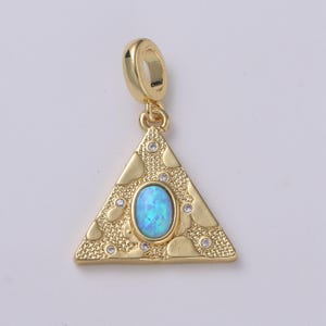 Puede incluir: Colgante dorado con forma triangular y un lazo en la parte superior. El colgante presenta una piedra ovalada azul claro en el centro, rodeada de pequeñas piedras transparentes y una superficie texturizada. Una joya elegante.