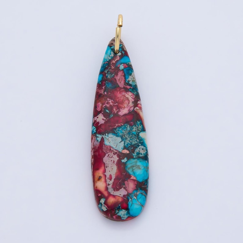 May include: A teardrop-shaped pendant with a gold-colored bail. The pendant features a mosaic pattern of red, blue, and cream-colored stone. The stone has a polished finish and is set against a white background.