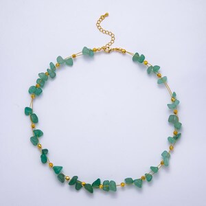 May include: A delicate necklace featuring small, irregular green gemstone beads strung on a thin gold-colored wire. The necklace has a gold-colored clasp and small gold-colored beads interspersed between the green stones. The necklace is designed to be worn around the neck.