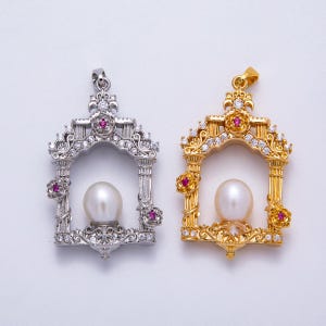 May include: Two ornate pendants, one silver-toned and one gold-toned, each featuring a large, lustrous pearl. The pendants have a decorative arch design with embedded gemstones and floral accents, showcasing intricate detailing.