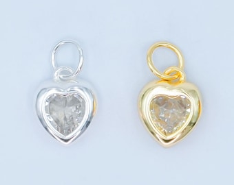 Puede incluir: Dos colgantes en forma de corazón. Uno es plateado, el otro dorado. Ambos tienen una piedra transparente en forma de corazón en el centro. Cada colgante tiene un pequeño lazo en la parte superior para sujetarlo a una cadena o pulsera.