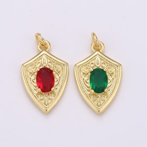 May include: Two gold-tone pendant charms in the shape of a shield with an ornate design. One charm features a red oval-shaped gemstone, and the other charm features a green oval-shaped gemstone.