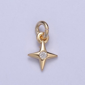 Könnte beinhalten: Ein goldener Anhänger in Form eines vierzackigen Sterns mit einem klaren Strassstein in der Mitte. Der Anhänger hat eine Öse oben zum Anbringen an einem Armband oder einer Halskette.