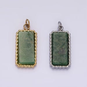 May include: Two rectangular pendants with a green stone set in a gold and silver frame. The pendants have a beaded border.