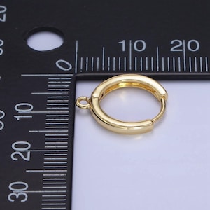 May include: A gold-coloured hoop earring with a hinged closure and a small loop for attachment. The earring is shown against a white and black background with a ruler for scale. The earring is approximately 1.9 cm in diameter.
