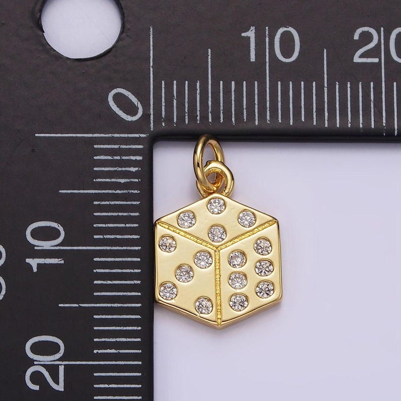 Pu&ograve; includere: Un ciondolo a forma di dado dorato con accenti di cristallo trasparente. Il ciondolo ha la forma di un cubo con sei lati, ognuno adornato con punti di cristallo che rappresentano i numeri su un dado. Il ciondolo &egrave; attaccato a un piccolo anello per essere appeso.