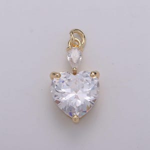 May include: A gold pendant featuring a large, clear heart-shaped crystal with a smaller, teardrop-shaped crystal above it.