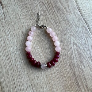 May include: A pink and burgundy beaded bracelet with a silver clasp and a larger pink bead in the center.