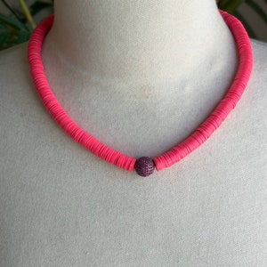 May include: A pink beaded necklace with a sparkly purple bead in the centre.