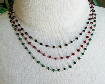 May include: A layered necklace with three strands of beads. The top strand is made of dark blue beads, the middle strand is made of red beads, and the bottom strand is made of green beads.
