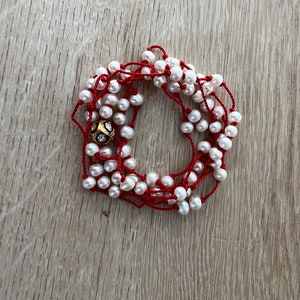 May include: A white pearl necklace with a gold and diamond bead accent, strung on a red cord.