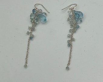 May include: A pair of silver dangle earrings with a cluster of light blue and clear teardrop-shaped crystals hanging from each earring.