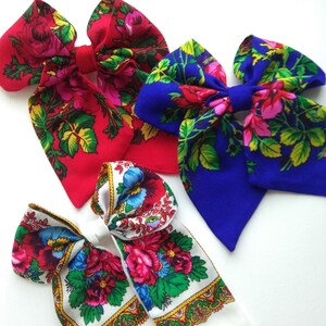 May include: Three fabric hair bows with floral patterns. The bows are red, blue, and white with a variety of floral designs.
