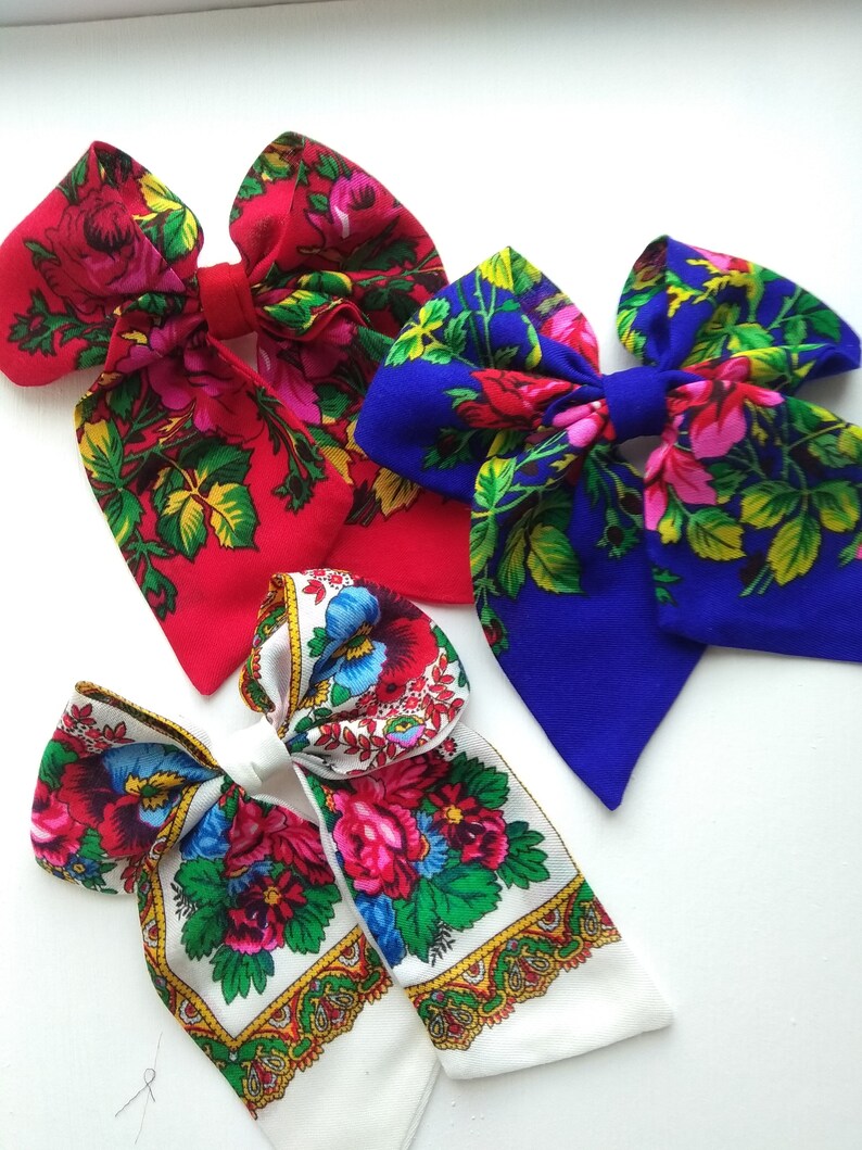May include: Three fabric hair bows with floral patterns. The bows are red, blue, and white with a variety of floral designs.