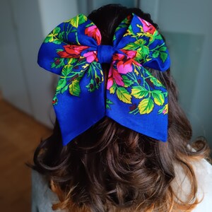 May include: A large blue bow with a floral pattern in shades of pink, yellow, and green. The bow is tied at the back of a person's hair.
