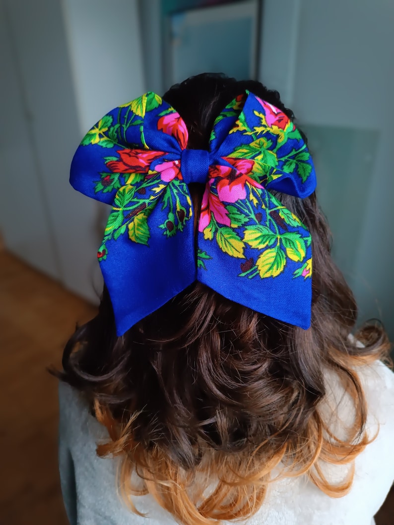 May include: A large blue bow with a floral pattern in shades of pink, yellow, and green. The bow is tied at the back of a person's hair.