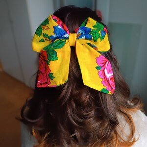 May include: A yellow bow with a floral pattern in pink, blue, and green. The bow is tied at the back of a person's hair.