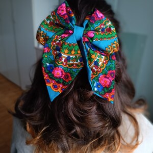 May include: A blue bow with a floral pattern in shades of pink, green, yellow, and white. The bow is tied in a person's hair.