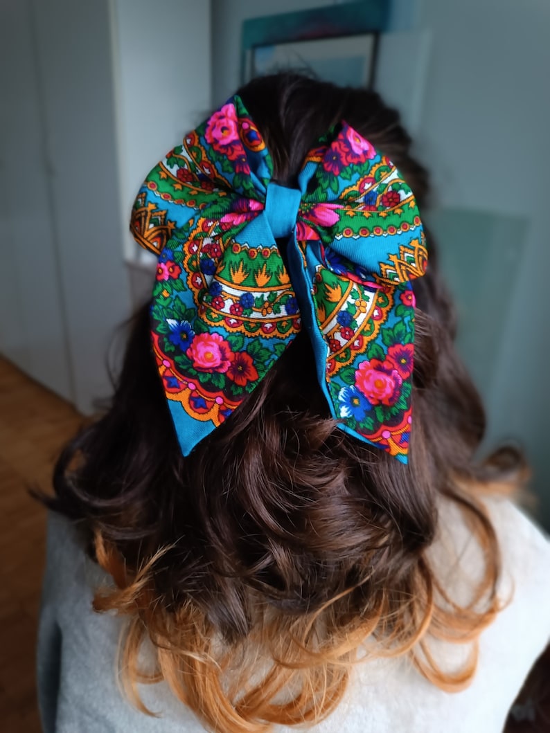 May include: A blue bow with a floral pattern in shades of pink, green, yellow, and white. The bow is tied in a person's hair.
