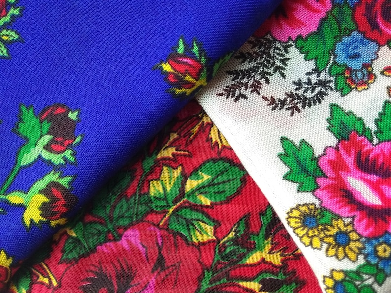 May include: Three fabric swatches with floral patterns. The first swatch is a solid blue with red and yellow flowers. The second swatch is red with green leaves and pink flowers. The third swatch is white with green leaves and pink, yellow, and blue flowers.