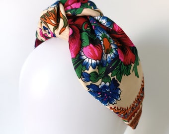 May include: A knotted headband with a floral pattern in shades of pink, blue, green, orange, and yellow on a cream background.
