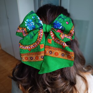 May include: A green fabric bow with a colourful floral pattern. The bow is tied in a large knot and has a red, orange and yellow border.