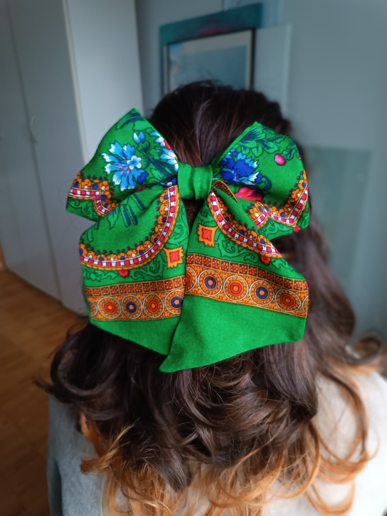 May include: A green fabric bow with a colourful floral pattern. The bow is tied in a large knot and has a red, orange and yellow border.