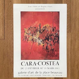 May include: A red and white poster advertising an art exhibition by Cara-Costea at the Galerie d'Art de la Place Beauvau in Paris. The poster features an abstract painting of a crowd of people in a red room. The exhibition dates are from February 23rd to March 19th, 1983.