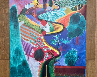 Può includere: Un poster colorato per una retrospettiva di David Hockney al Metropolitan Museum of Art. Il poster presenta un dipinto di paesaggio vibrante con una strada tortuosa, case e alberi in tonalità di blu, verde, giallo, arancione e rosso. Il testo "David Hockney: A Retrospective" e "The Metropolitan Museum of Art" è stampato nella parte inferiore del poster.